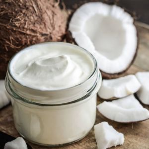 Whipped coconut shea butter in glass jar surrounded by broken coconuts