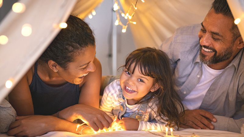 Father, mother, and child playing in lighted tent