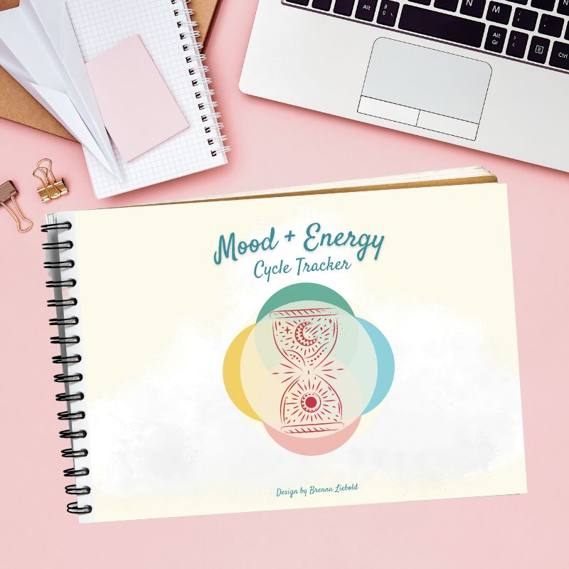 Mood + Energy Cycle Tracker cover mockup notepad on pink desk next to laptop.